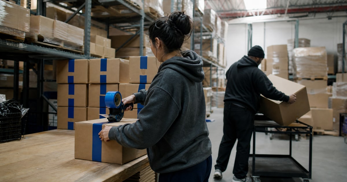 Flapen cover for Amazon account suspension help services: a Flapen operator sealing a carton with blue tape beside a stack of sealed ones