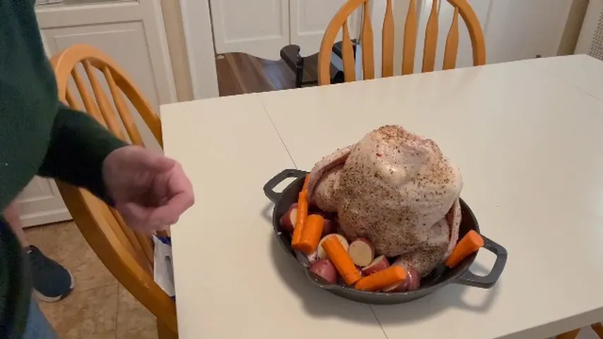 A whole chicken on the vertical roaster with carrots and potatoes
