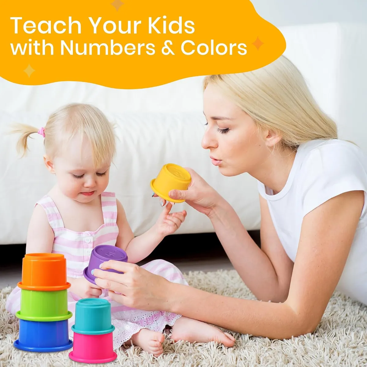 Mother holding a yellow cup while a toddler in a pink striped dress plays with stacked colorful cups on a rug