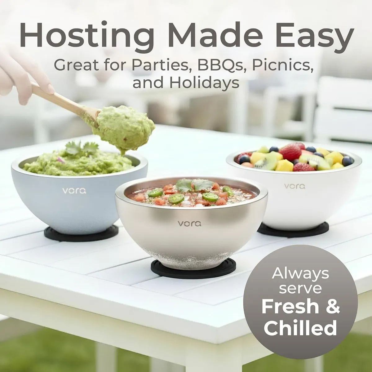 Hand spooning guacamole from a blue Vora bowl on an outdoor table, next to a stainless bowl of salsa and a white bowl of fruit salad