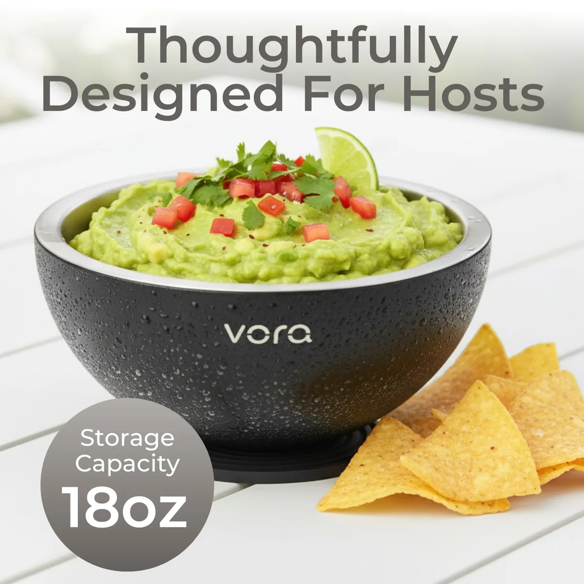 Close-up of a condensation-beaded black Vora bowl of guacamole with lime and tortilla chips on a white outdoor table